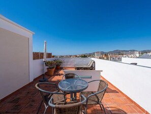 Eine Dachterrasse mit Tisch und Stühlen, Blumentöpfen und Blick auf die Stadtlandschaft.
