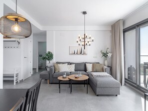 Una sala moderna con un sofá gris, dos mesas redondas de centro, una lámpara colgante y un cuadro de veleros en la pared.