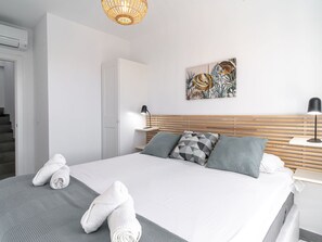 Ein modernes Schlafzimmer mit Bett, Kissen, einem Nachttisch, einer Lampe, einem Gemälde und einer Treppe.