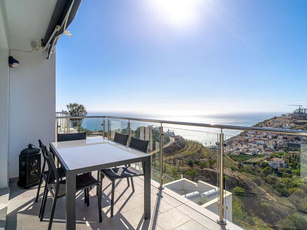 Ein Balkon mit Tisch und Stühlen mit Blick auf eine Küstenstadt und das Meer.