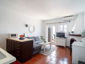 Ein kompakter Wohnraum mit Küchenzeile, einem grauen Sofa, einem Couchtisch und einem Fernseher.
