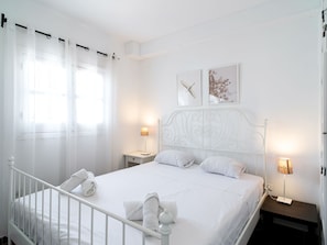 Ein weißes Himmelbett mit zwei Nachttischen, jeweils mit einer Lampe, in einem Zimmer mit weißen Wänden und Vorhängen.