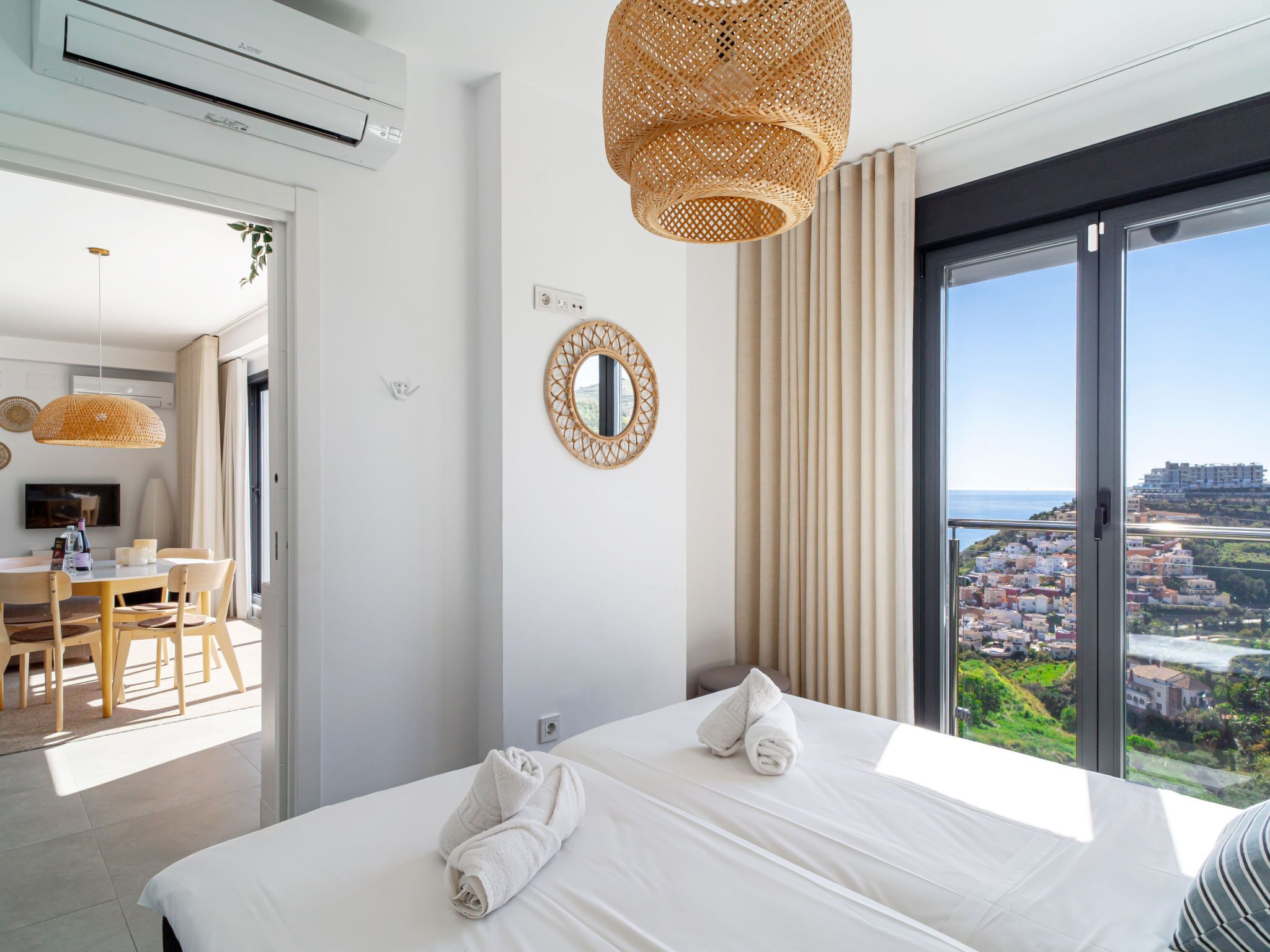 A hotel room with a bed, a dining area, a view of the city, and a large window.