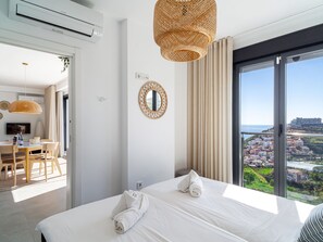 Ein Hotelzimmer mit Bett, Essbereich, Blick auf die Stadt und einem großen Fenster.