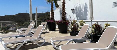 A rooftop terrace with lounge chairs, potted plants, and a view of the landscape.
