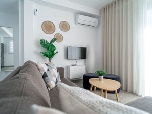 Ein modernes Wohnzimmer mit einer Couch, einem kleinen runden Tisch, einem Fernseher und einer Topfpflanze.