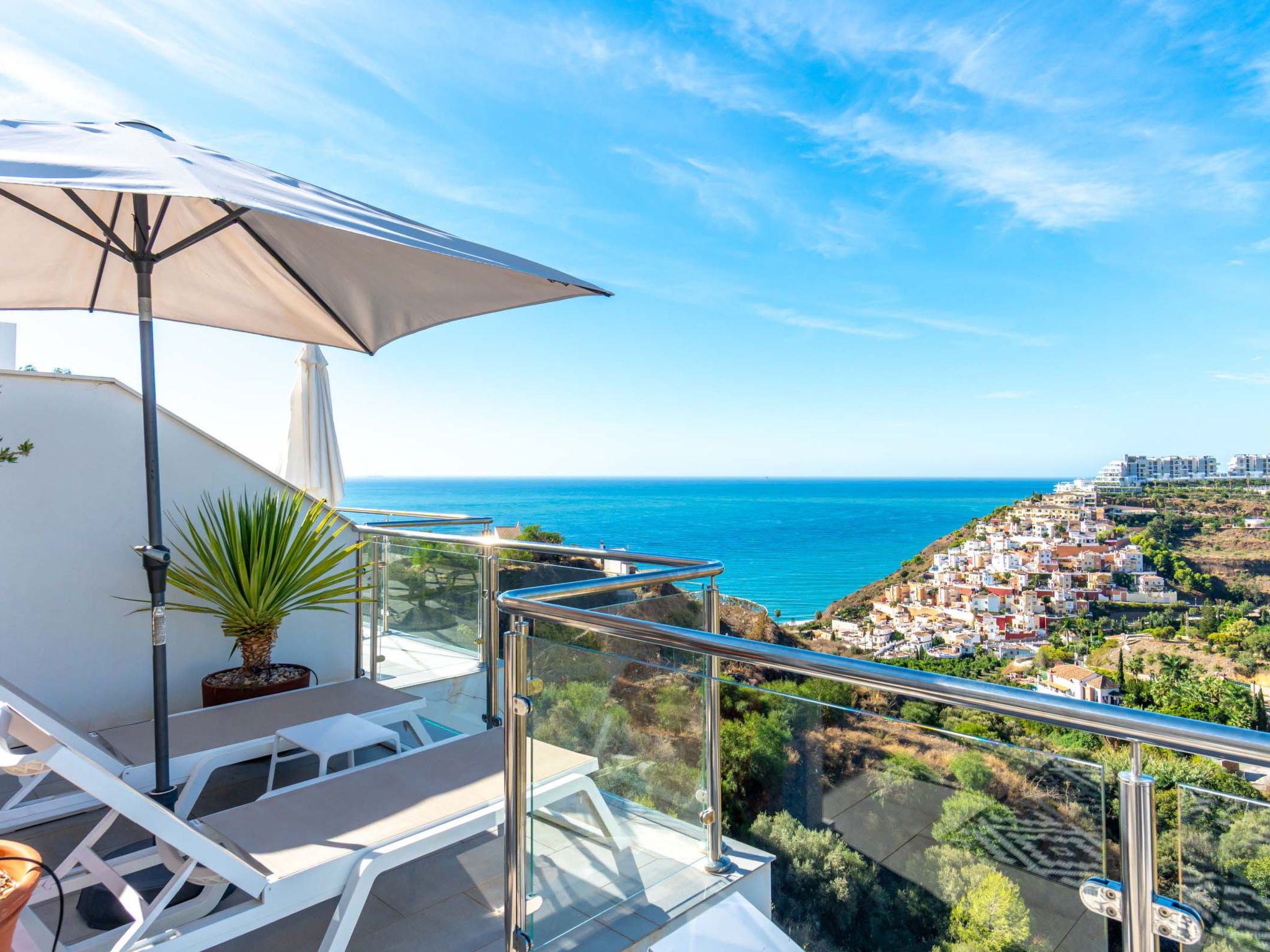 A balcony with a view of the sea, a potted plant, and outdoor furniture.