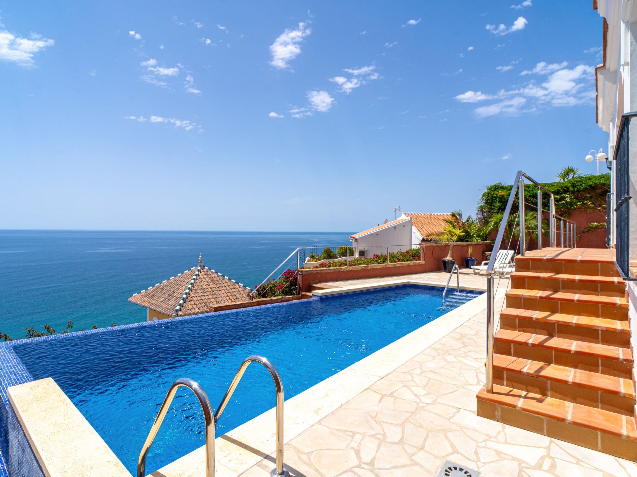 Uma piscina com vista para o mar, uma escadaria e um edifício com telhado em azulejos.