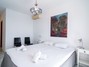 Hotellihuone, jossa on suuri sänky, kaksi tuolia, työpöytä, pöytälamppu, seinälle ripustettu taulu ja kattovalaisin.