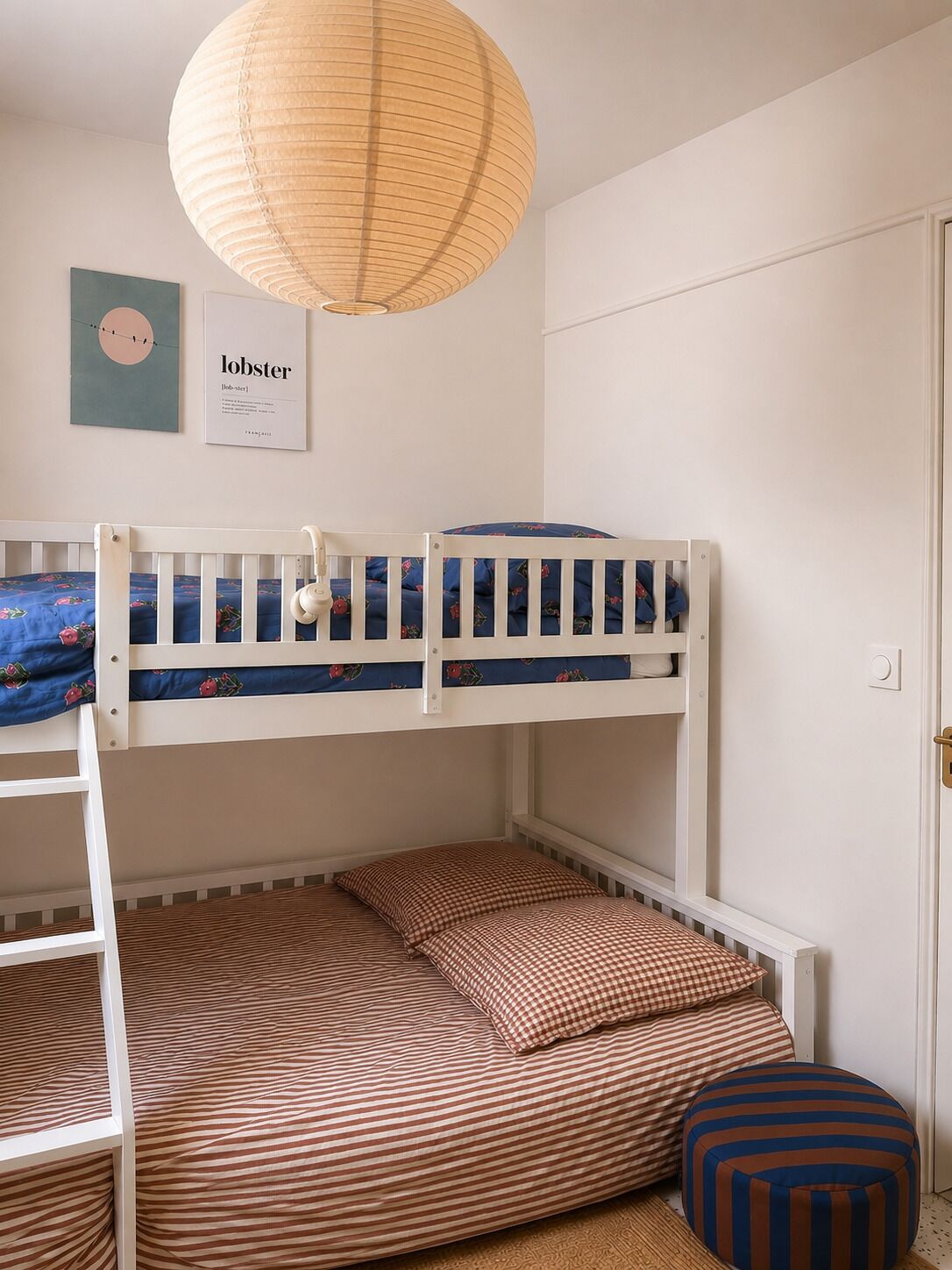 Un lit superposé avec une échelle, une lampe suspendue et un livre encadré accroché au mur.