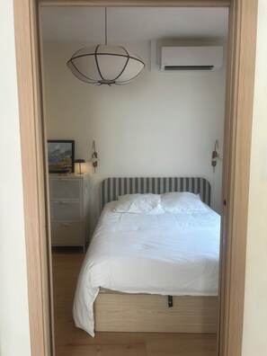 A bedroom with a bed, a hanging light fixture, an air conditioning unit, a bedside table with a lamp, and a wall-mounted picture. - Royan-Pontaillac – House a 5-minute walk from the beach, with a patio and air conditioning (Royan)