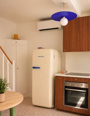 A compact kitchen with a white refrigerator, a wooden cabinet, a built-in oven, and a ceiling light fixture. - Royan-Pontaillac – House a 5-minute walk from the beach, with a patio and air conditioning (Royan)