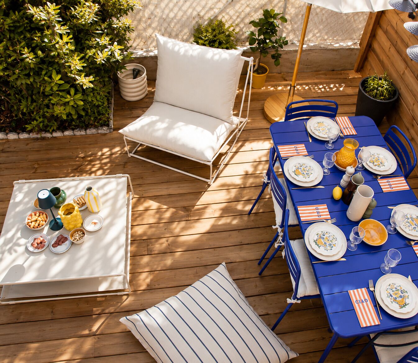 Une terrasse extérieure avec une table à manger pour quatre personnes, entourée de chaises bleues et d’un fauteuil blanc avec coussin.