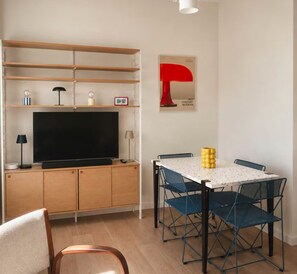 A modern living room with a flat-screen TV, wooden cabinets, a dining table with blue chairs, and a red abstract painting. - Royan-Pontaillac – House a 5-minute walk from the beach, with a patio and air conditioning (Royan)