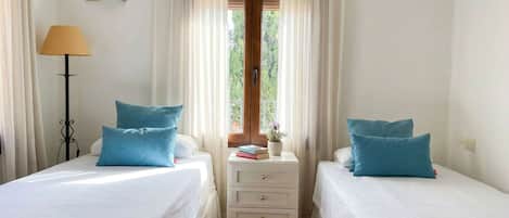 A room with two beds, a nightstand with drawers, a lamp, and a window with curtains.