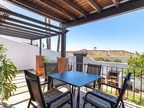 Eine Terrasse im Freien mit Tisch und Stühlen, einer Pergola und Blick auf ein traditionelles Gebäude.