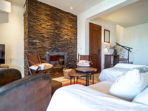 Ein gemütliches Wohnzimmer mit Steinwand, Kamin, einer Couch, einem Sessel und einem kleinen Tisch.