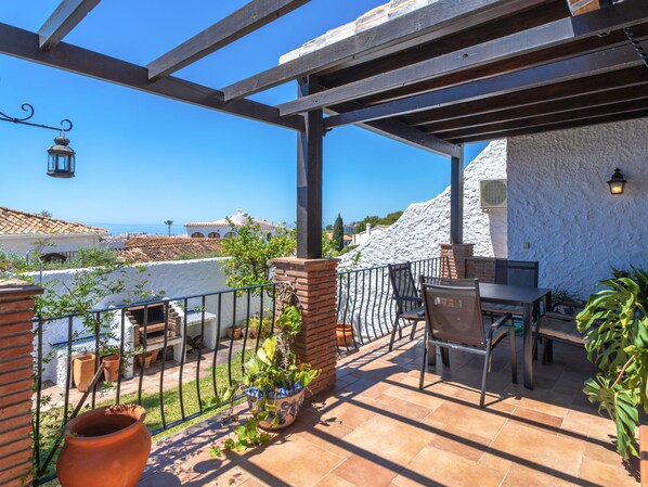 Eine Terrasse mit Tisch und Stühlen, einer Pergola, Topfpflanzen und Blick aufs Meer.