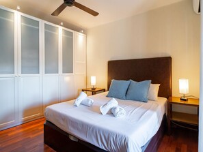 A hotel room with a bed, two bedside tables with lamps, a ceiling fan, and a wardrobe with frosted glass doors. - Capistrano Village Casa Garden by Interhome (Nerja)