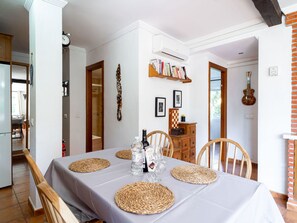 Un coin repas avec une table dressée pour quatre personnes, entourée de chaises, et agrémenté d’une bibliothèque et d’une guitare accrochée au mur.