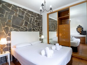 Une chambre d’hôtel avec un mur en pierre, un grand lit avec du linge de lit blanc, une armoire en bois et un miroir.