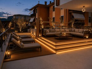A modern outdoor living area with a sofa set, lounge chairs, and a coffee table, surrounded by plants and ambient lighting. - NEW: Casa Jasmina - Residence Corte Carden 2 (Bardolino)