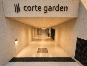 Un couloir avec une pancarte indiquant « jardin de la cour », qui mène à un espace d’accueil doté d’un sol à motifs et d’une plante en pot.