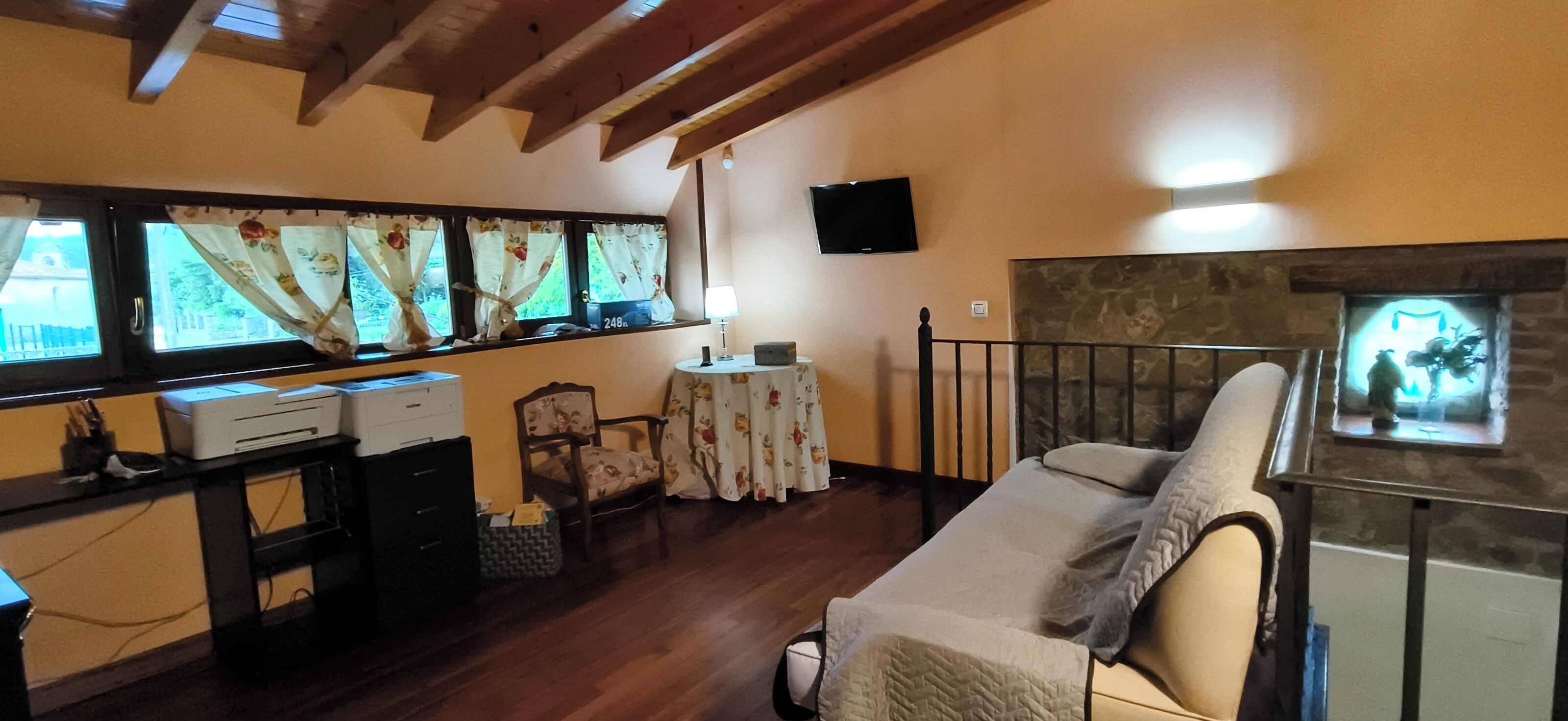 A room with a bed, a desk with printers, a chair, a table, a TV, and a fireplace.