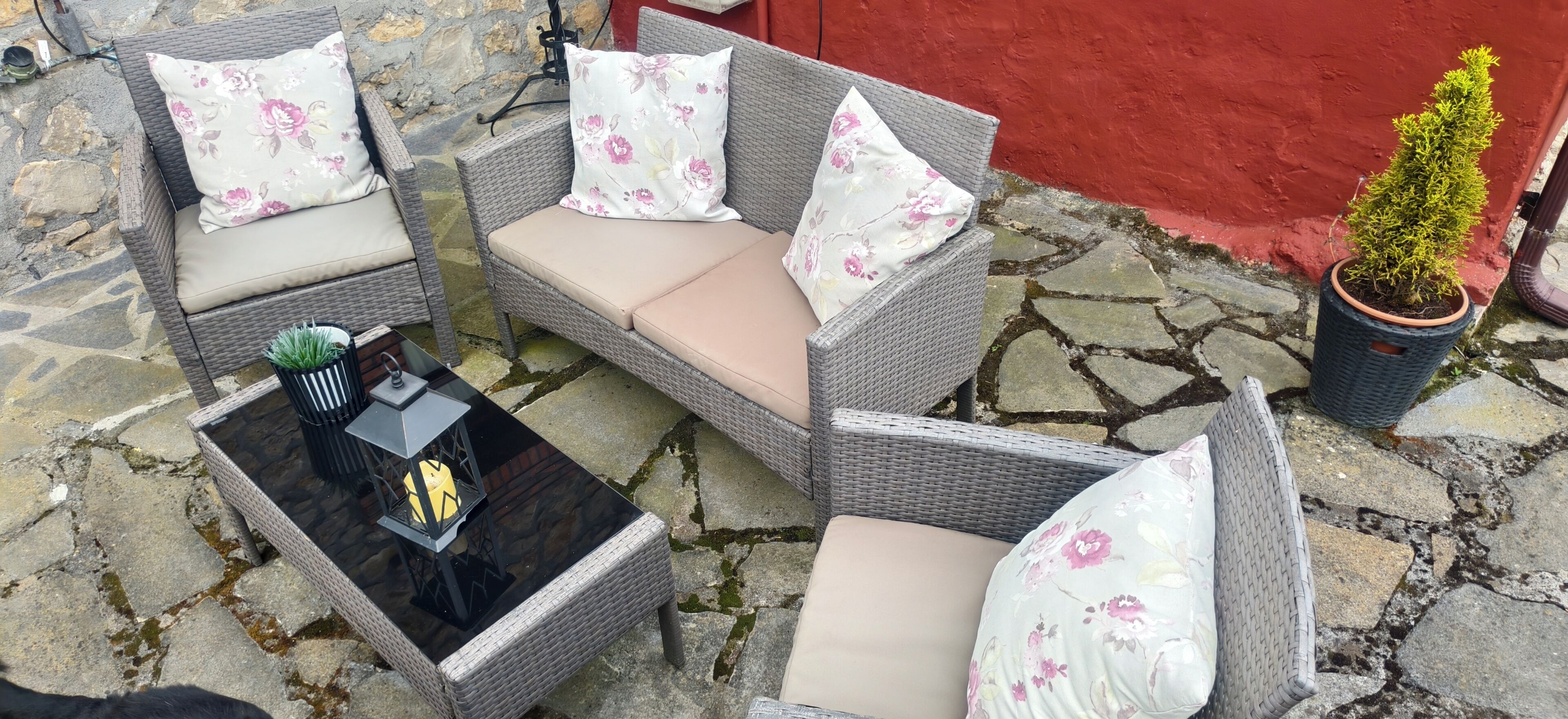 Een zithoek van riet, met kussens en een tafel, op een stenen terras.
