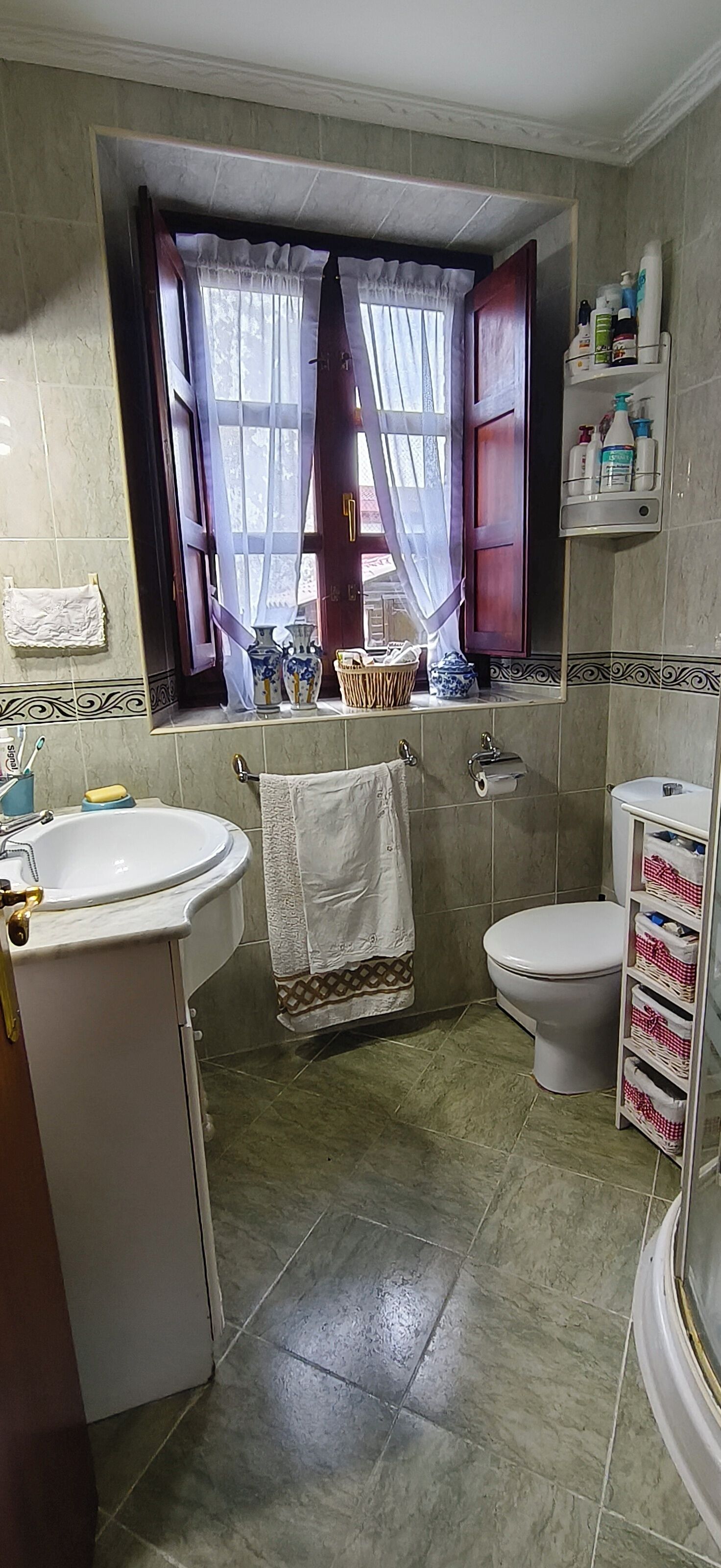 Un bagno con lavandino, WC e finestra con tende.