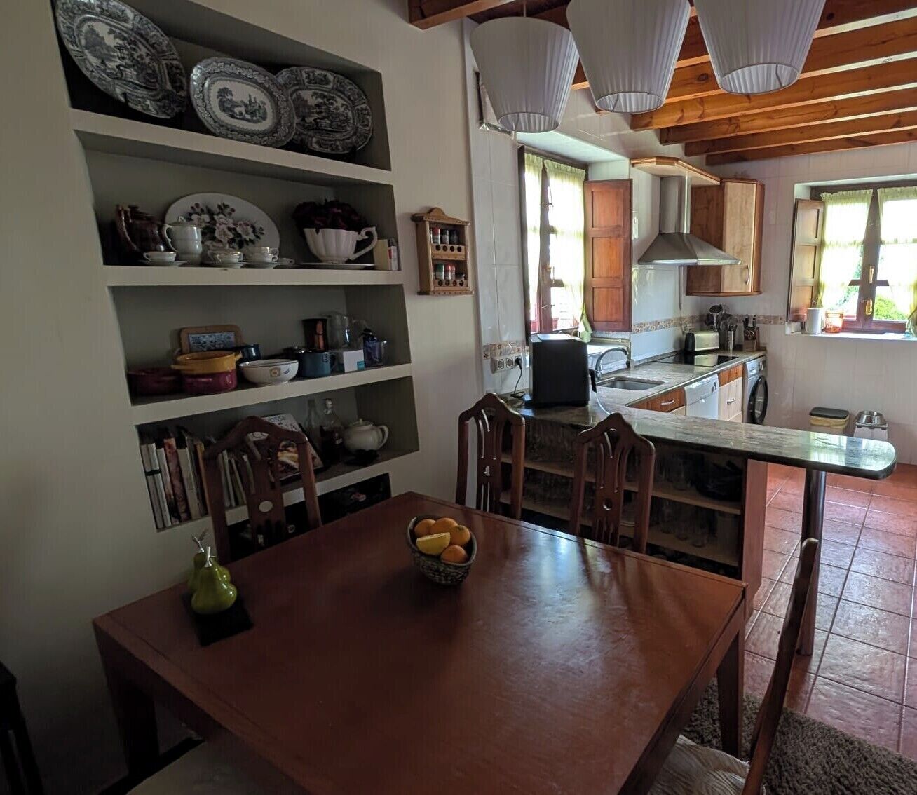 Un coin repas avec une table et des chaises en bois, une cuisine équipée d’une cuisinière et de placards, et une étagère ornée d’assiettes décoratives.