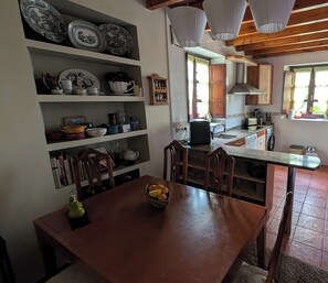 Un coin repas avec une table et des chaises en bois, une cuisine équipée d’une cuisinière et de placards, et une étagère ornée d’assiettes décoratives.