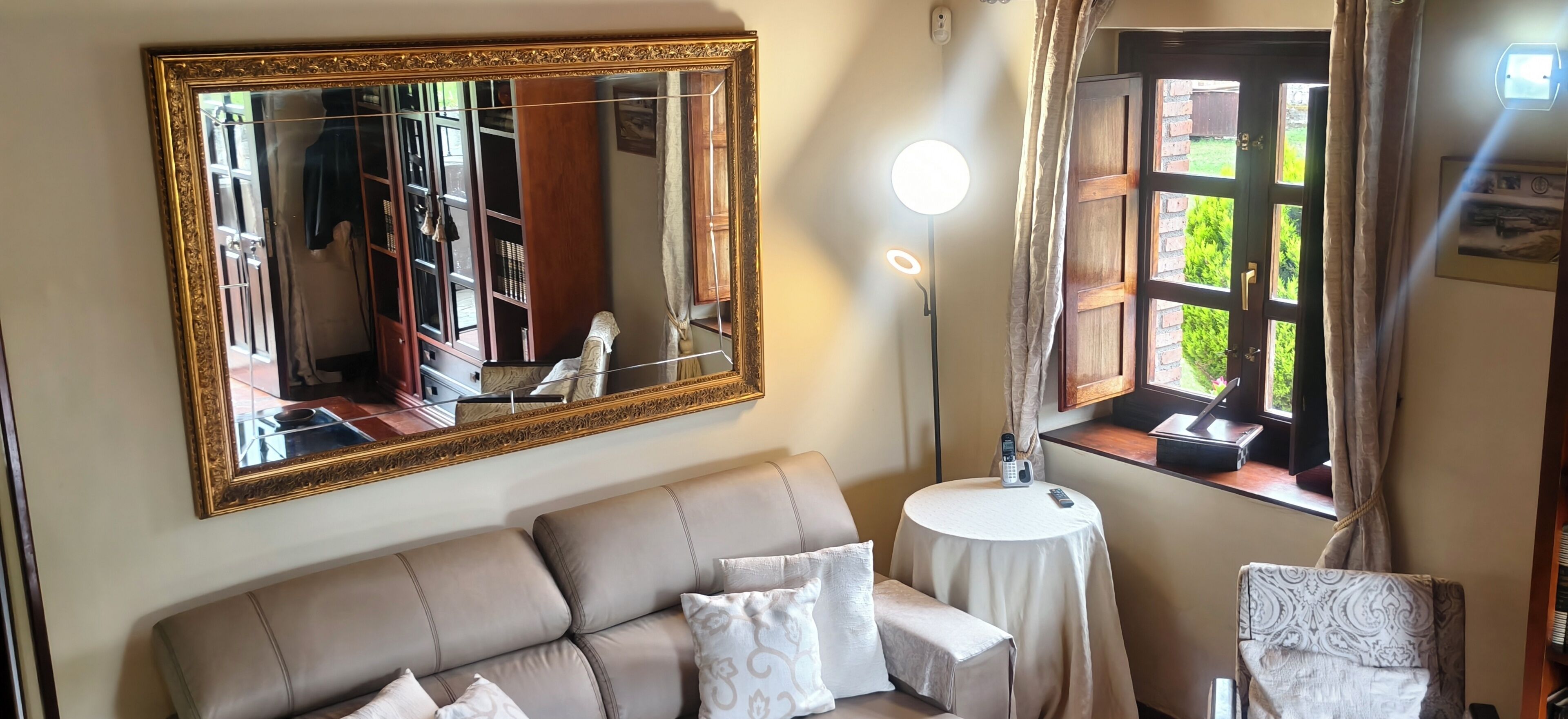 A living room with a large mirror, a sofa, a round table, and a window with curtains.
