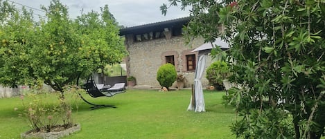 A stone building with a lawn, a swing chair, and a potted plant.