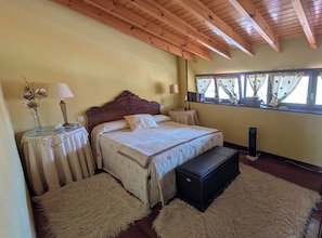 A bedroom with a wooden ceiling, a bed with a headboard, bedside tables, a window with curtains, and a bedside lamp.