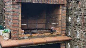 Un horno de ladrillo al aire libre con puerta negra, rodeado por una cerca de cadena y un muro de piedra con aberturas circulares.