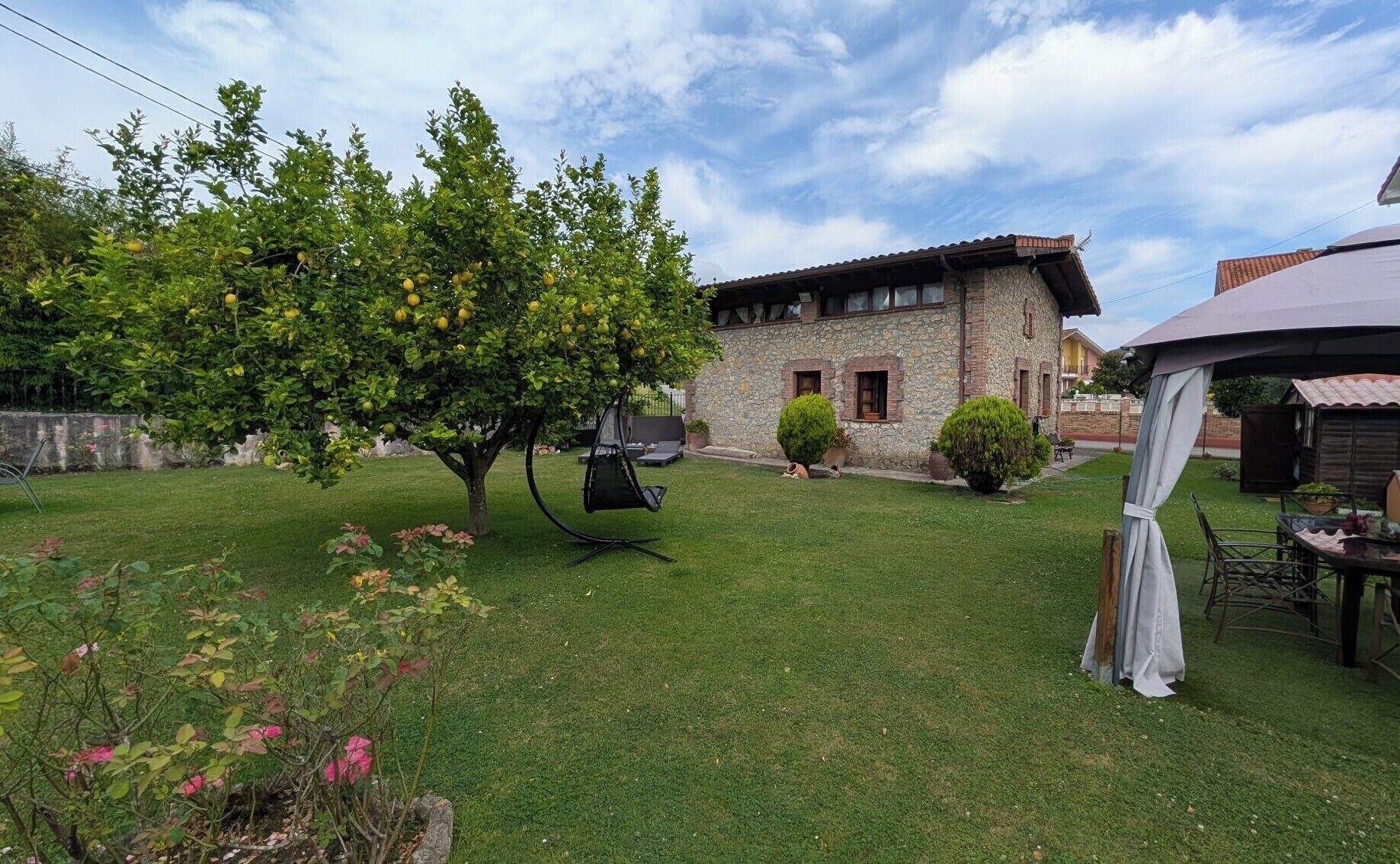 Una casa de piedra con jardín, columpio y porche cubierto.