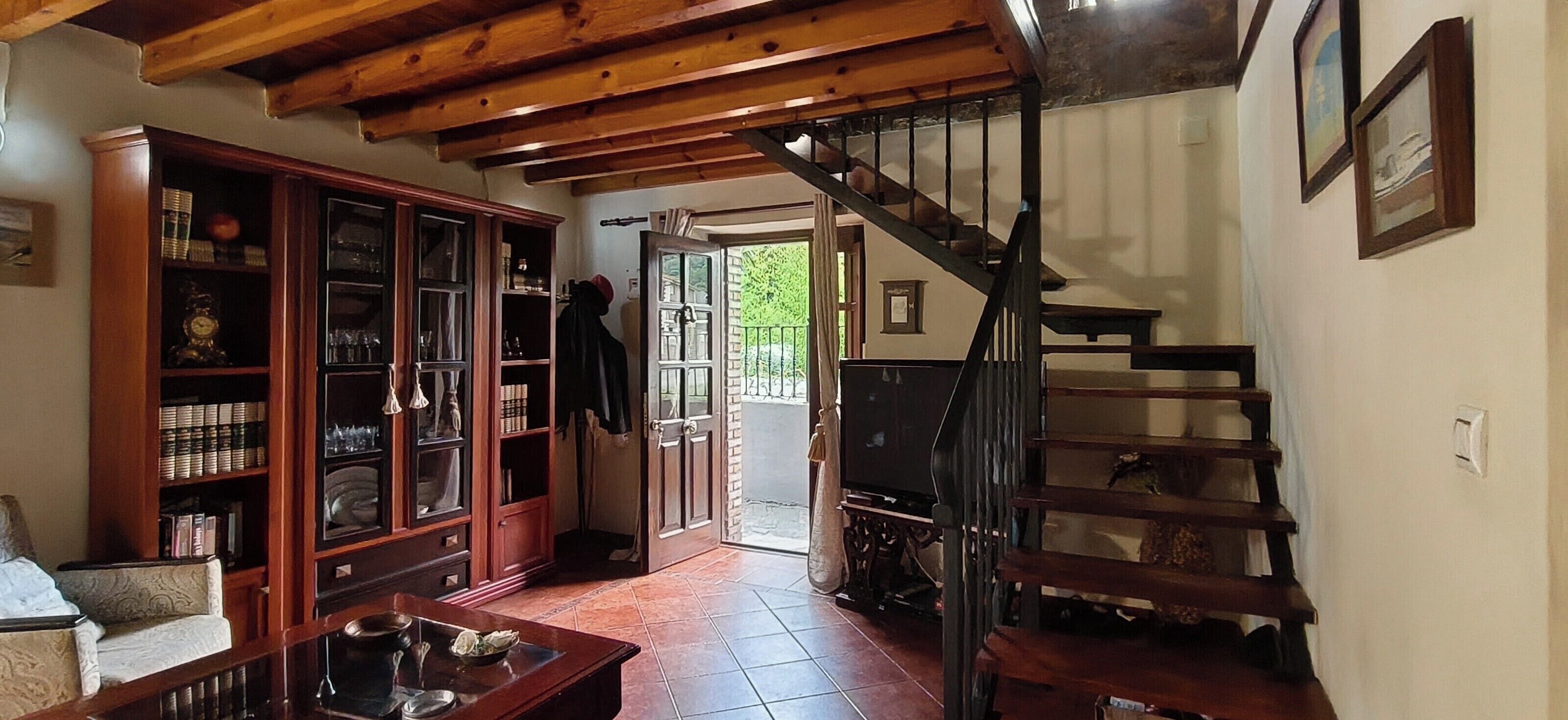 Una stanza con una scala in legno, una libreria e una porta che dà sull'esterno.