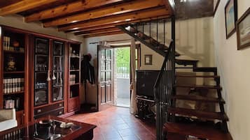 Una stanza con una scala in legno, una libreria e una porta che dà sull'esterno.