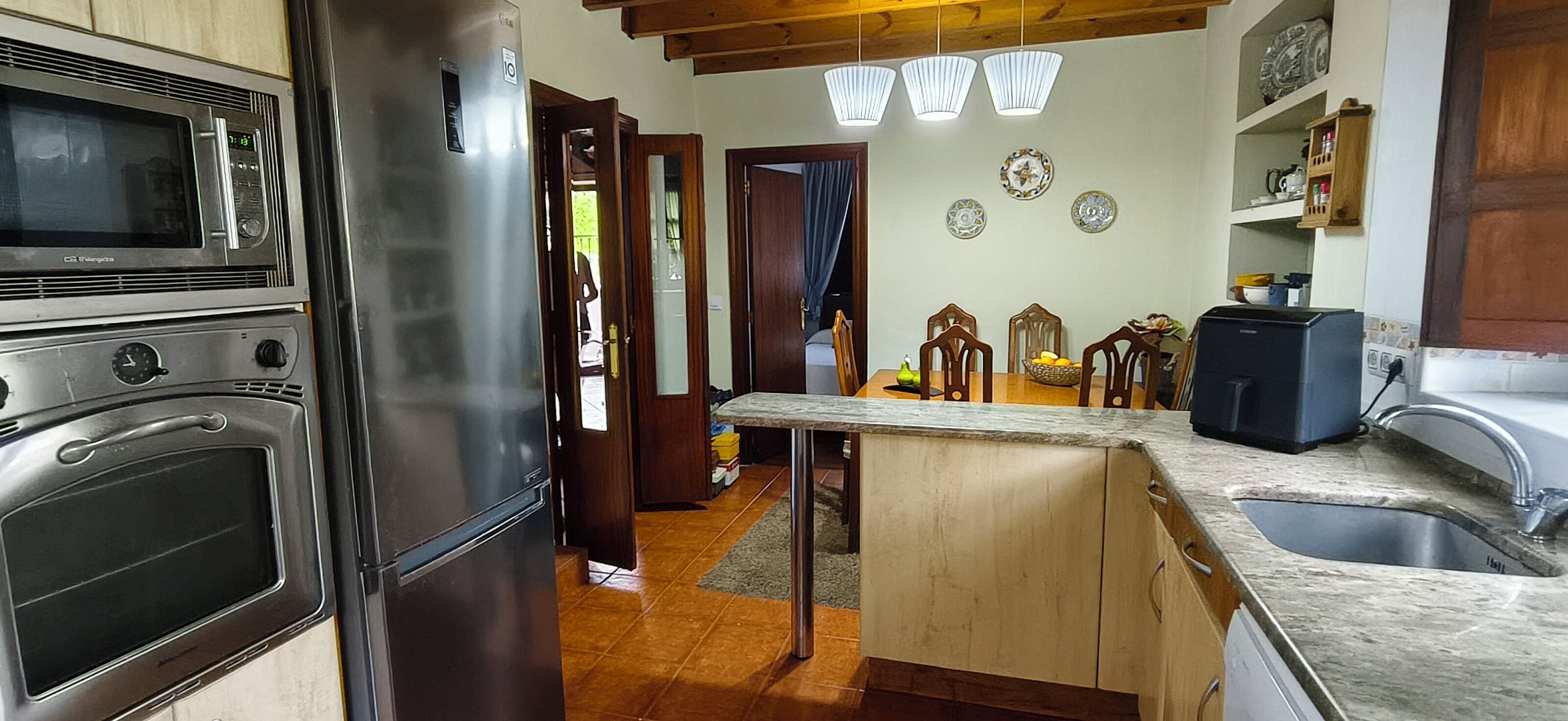 Cocina con refrigerador de acero inoxidable, microondas y cafetera. Hay una mesa de comedor de madera con sillas y una pequeña isla con un lavamanos.