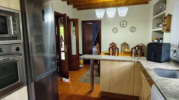 Cocina con refrigerador de acero inoxidable, microondas y cafetera. Hay una mesa de comedor de madera con sillas y una pequeña isla con un lavamanos.