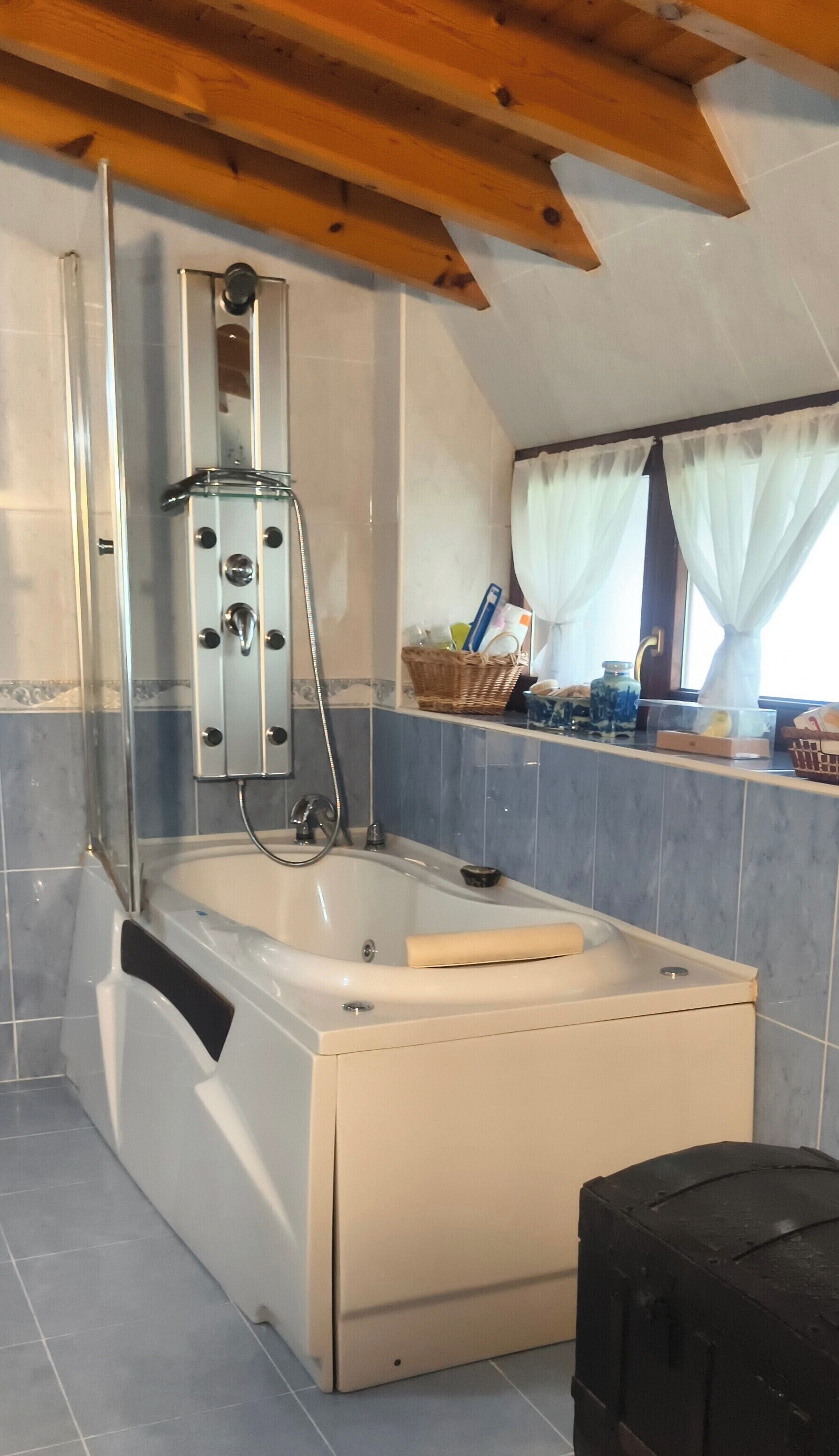 A bathroom with a bathtub, a shower, and a window with curtains.