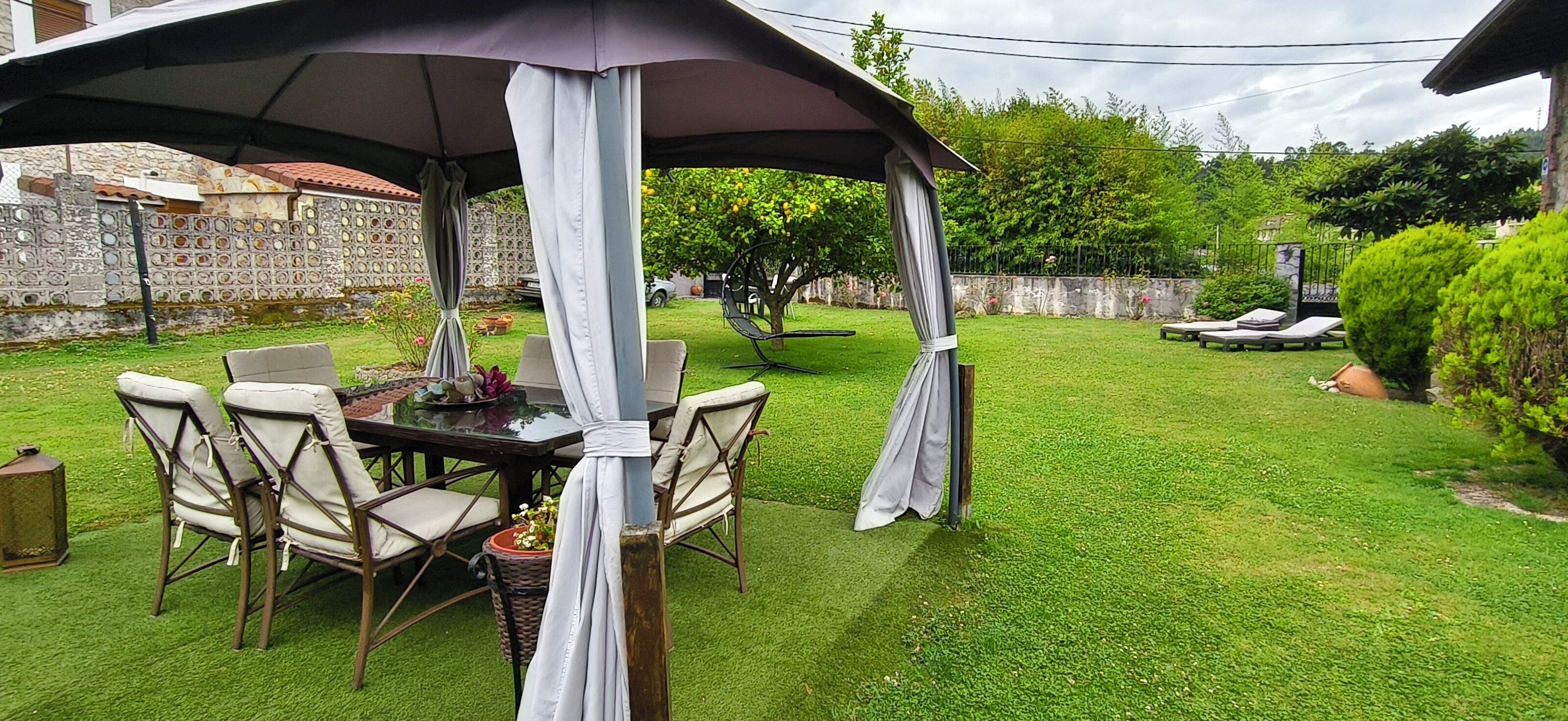 Un patio esterno con tavolo e sedie, circondato da un prato e un muro in pietra.