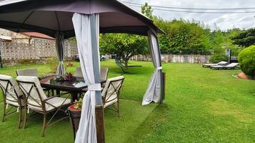 Un patio esterno con tavolo e sedie, circondato da un prato e un muro in pietra.