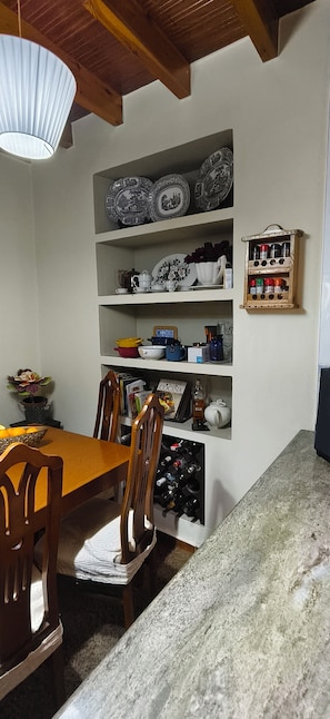 A dining area with a wooden table and chairs, a shelf with kitchenware, and a spice rack.