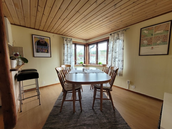 A dining area with a wooden table, four chairs, a rug, and a window with curtains.