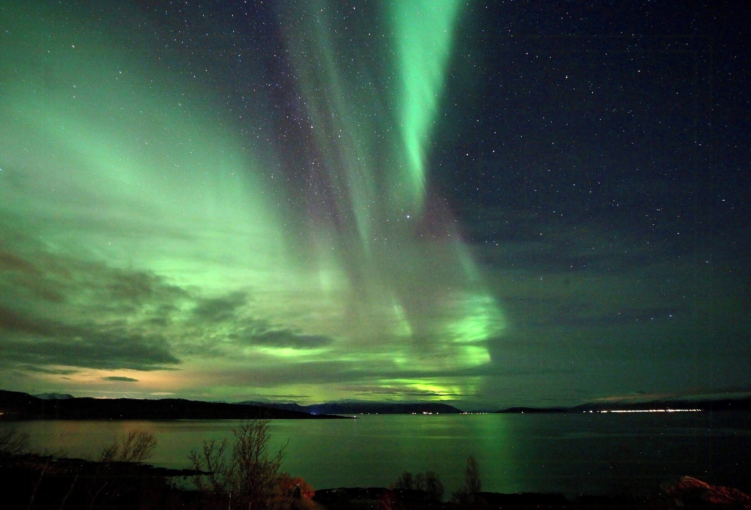 Cielo nocturno con la aurora boreal sobre un cuerpo de agua tranquilo.