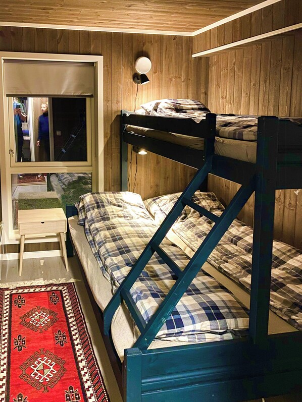 A bunk bed with a headboard, a bedside table, a mirror, and a window with blinds.