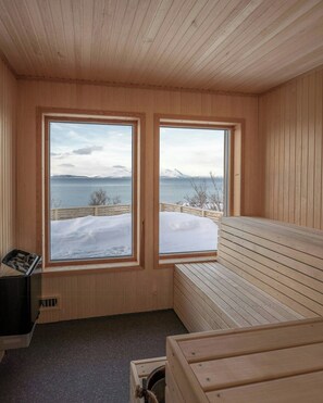 A wooden sauna room with two large windows offering a view of a snowy landscape and a body of water.