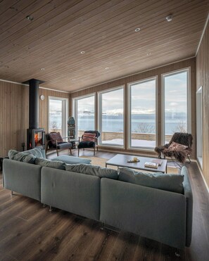 A modern living room with a large sofa, a fireplace, and a view of a body of water through large windows.